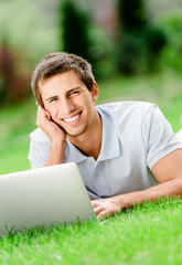 Man lying on the green grass works at the silver laptop