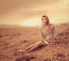 beautiful young woman sitting on hay. The picture shows a sunset