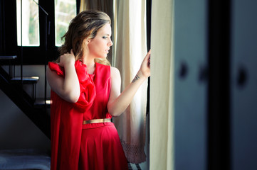 Fototapeta na wymiar Beautiful blonde woman in window wearing a red dress