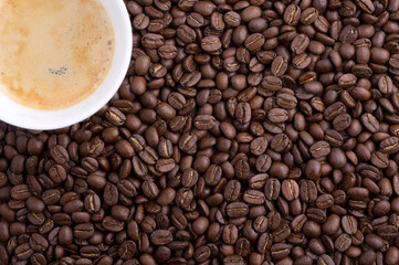 White cup of coffee with coffee beans scattered