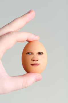 Male hand holding egg with human face