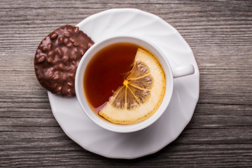 Hot cup of tea in white mug with lemon and chocolate cookie.