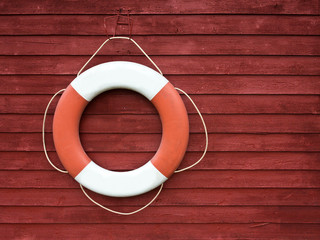 Red and white life buoy hanging on the side of a wooden ship