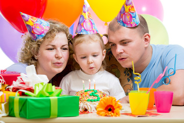 kid girl with parents blow candles on birthday cake