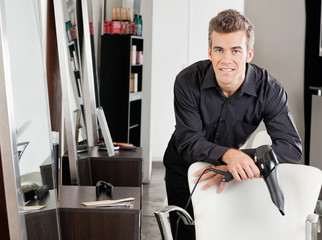 Male Hairstylist With Hairdryer Leaning On Chair