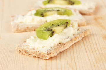 Tasty canapes with cheese and kiwi, on wooden background