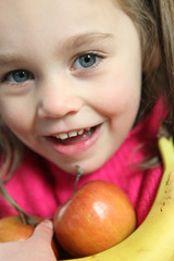 Little girl holding apples and banana