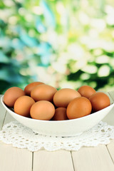 Eggs in white bowl on wooden table on natural background