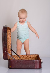 baby girl playing with suitcase on grey background