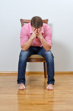 Depressed man sitting on a chair against the wall
