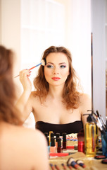 Young beautiful woman making make-up near mirror