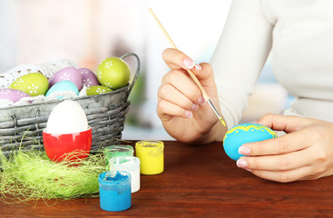 Fototapeta na wymiar Young woman painting Easter eggs, on bright background
