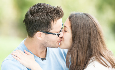 Pretty woman and man in glasses kissing in park.