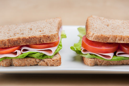 Ham sandwiches with tomatoes and lettuce on the white plate.