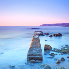 Concrete pier or jetty and rocks on a blue sea. Hills on backgro © stevanzz