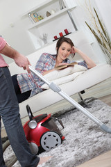 Husband vacuuming whilst wife lays on sofa