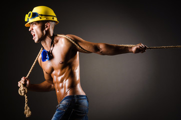 Nude builder pulling rope in darkness