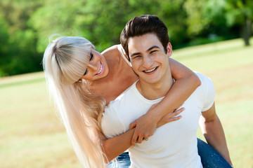 Obraz premium Handsome couple piggybacking in park.