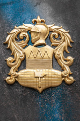 Gold arms with knight image on granite wall.