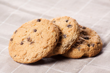 Stacked chocolate chip cookies on brown napkin.
