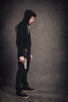 Young killer with gun portrait over dark grunge background. 
