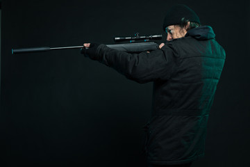 Sniper with beard in black holding gun. Studio shot.