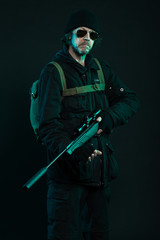 Sniper with beard in black holding gun. Studio shot.