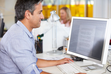Man Working At Desk In Busy Creative Office