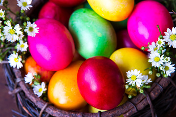 Fototapeta na wymiar Colorful easter eggs in brown basket with flower