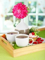Cups of tea with flower and cake on wooden tray on table in