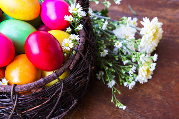 Colorful easter eggs in brown basket with flower