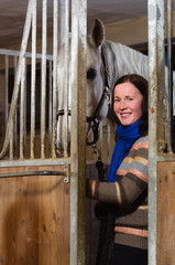 Smiling woman and white horse inside a stall, vertical format