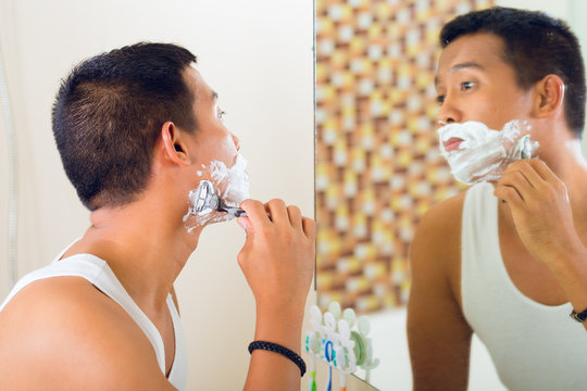 Asian Man Shaving In Front Of Mirror