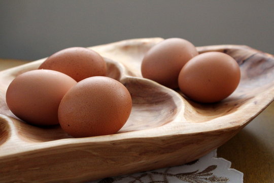 Five fresh brown eggs on wood platter
