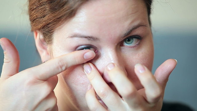 Young woman inserting blue contact lens in eye