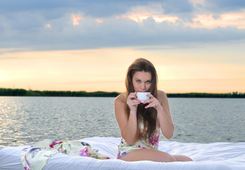 The girl woke up in a bed on water and drink cup of coffee