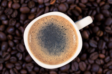 A cup of coffee is on the background of roasted coffee beans