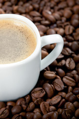 A cup of coffee is on the background of roasted coffee beans