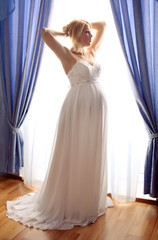 Beautiful pregnant bride posing against window