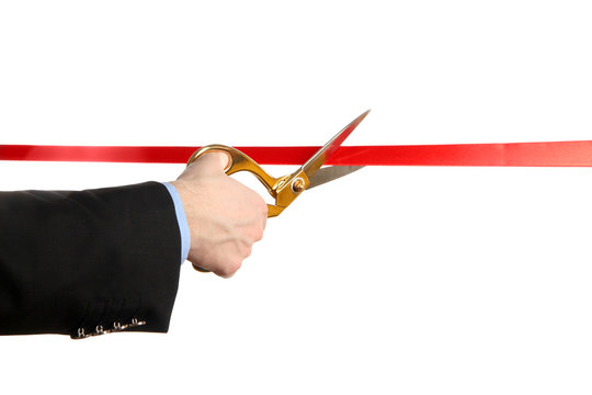Man's hand cutting red ribbon with pair of scissors isolated