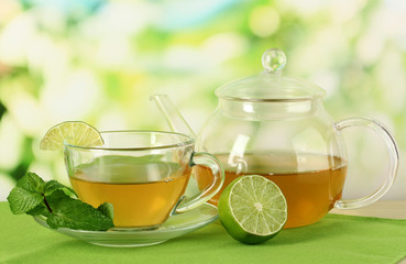 Cup of tea with mint and lime on table on bright background
