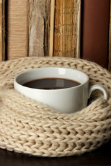 Cup of coffee wrapped in scarf on books background