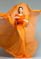 beautiful woman in long orange dress posing in the studio - 50081324