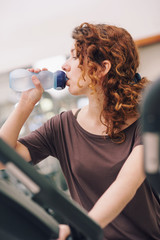 Young woman having a rest drinking a beverage in the gym.