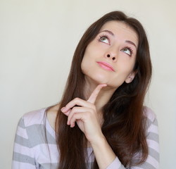 Smiling thinking woman looking up with finger at face isolated.