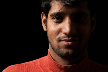 Portrait of young Indian man smiling over dark