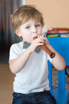 Little boy playing wooden flute indoor