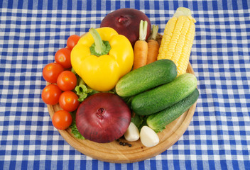 Vegetables on wooden cutting board on tablecloth