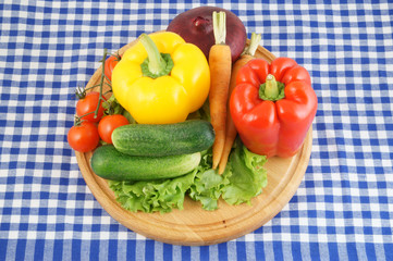 Vegetables on wooden cutting board on tablecloth