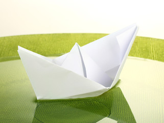 Color paper ship in water on green plate, close-up